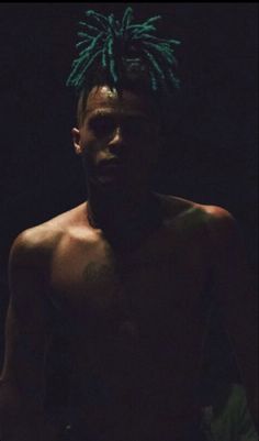 a shirtless man with green dreadlocks on his head and no shirt in the dark