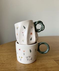 three ceramic cups sitting on top of a wooden table next to each other with handles