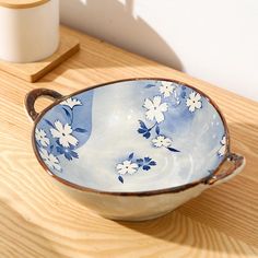 a blue and white bowl sitting on top of a wooden table next to a cup