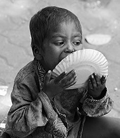 a young boy sitting on the ground holding a paper plate in front of his mouth