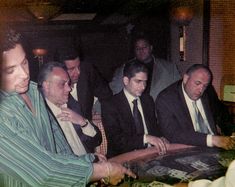 several men in suits sitting at a table with cards on it and one man holding his chin up