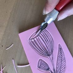 a person using a sharp knife to cut out paper flowers on a piece of pink paper