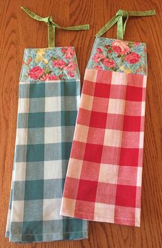 two pieces of cloth hanging on a wooden table with green ribbon and flowers in them