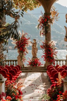 an outdoor ceremony setup with red chairs and flowers on the aisle, in front of a statue