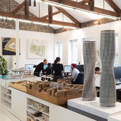 several people working in an office with stacks of boxes on the desk and two tall vases