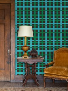 a chair and table in front of a wallpapered room with a lamp on it