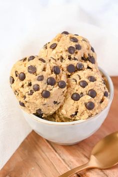 three chocolate chip cookies in a bowl next to a spoon on a wooden cutting board