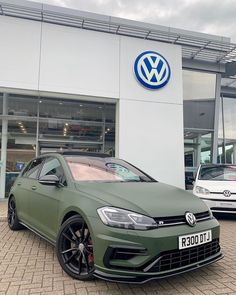 a green vw golf gti parked in front of a volkswagen dealers showroom