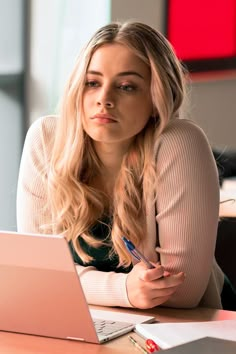 a woman sitting at a table with a laptop computer in front of her and writing