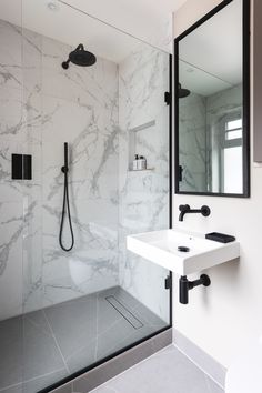 a bathroom with marble walls and flooring, black faucet shower head, white sink and mirror