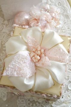 a white box with pink flowers and pearls on it sitting on a lace doily