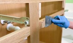 a person in blue gloves and rubber gloves holding a piece of wood to the side of a cabinet