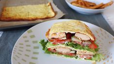 a sandwich cut in half sitting on top of a white plate next to a bowl of fries