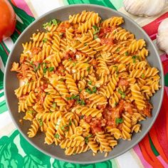 a bowl filled with pasta and sauce on top of a colorful table cloth next to garlic