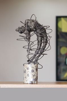 a metal wire sculpture sitting on top of a wooden table next to a framed painting