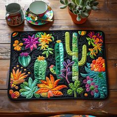 a place mat with colorful cactus and flowers on it next to two cups, mugs and saucers