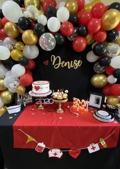 a red table topped with a cake and lots of balloons next to a sign that says denuse