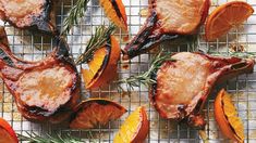 some meat and oranges on a cooling rack with rosemary sprigs around them