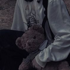 a man sitting on the ground holding a brown teddy bear in his lap and wearing a helmet