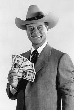 a black and white photo of a man wearing a cowboy hat holding money in one hand