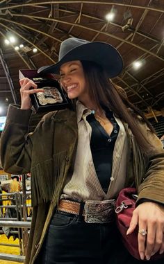 a woman wearing a cowboy hat and holding a cell phone up to her ear while standing in an arena