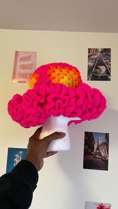 a person is holding up a crocheted hat on the wall with pictures around it