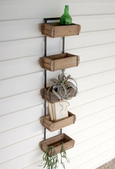 three wooden shelves holding books and plants on the side of a white building with a green bottle