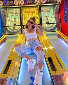 a woman sitting on top of a bowling alley talking on a cell phone while wearing white sneakers