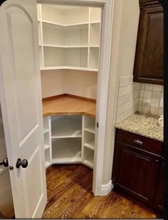 an empty pantry in the corner of a kitchen with wood floors and cabinets on either side