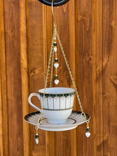 a teacup hanging from a chain on a wooden wall with beads and chains attached to it