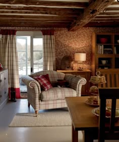 a living room filled with furniture next to a wooden table and window covered in curtains