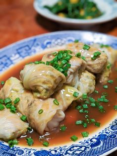 dumplings with sauce and green onions on a blue and white plate next to another dish