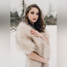 a woman is standing in the snow wearing a white fur stole with her hands on her chest