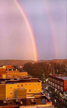 two rainbows in the sky over a city with cars parked on the street below