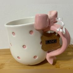 a pink and white ceramic cup sitting on top of a wooden table next to a tag