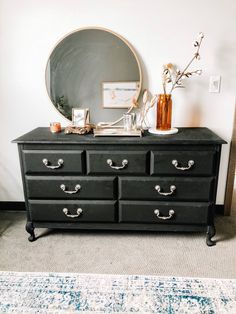 a black dresser with drawers and a mirror on it's top shelf next to a rug