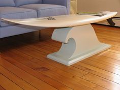 a surfboard shaped table sitting on top of a wooden floor next to a blue couch