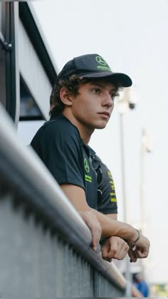 a young man wearing a black hat leaning against a railing