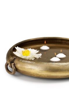 a brass tray with white candles and a flower on the bottom is shown in front of a white background