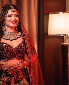 a woman in a red and gold bridal outfit with her hands on her hips