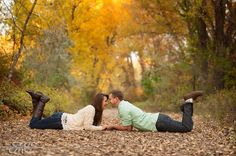 a man and woman laying on the ground in front of trees with their legs spread out