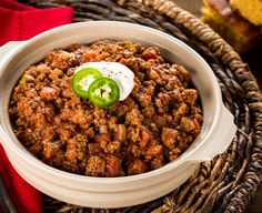 a white bowl filled with chili and topped with a green jalapeno slice