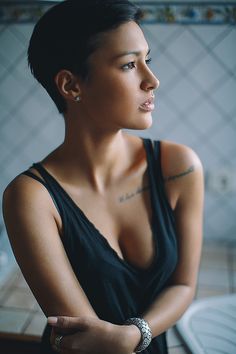 a woman with tattoos on her arm standing in front of a sink and looking off into the distance