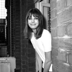 a black and white photo of a woman leaning against a brick wall in front of a door