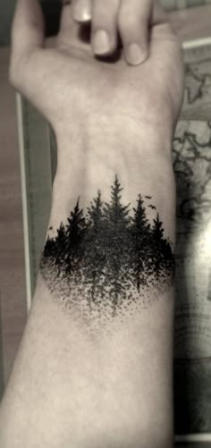 a person's arm with a forest tattoo on the left side of their wrist