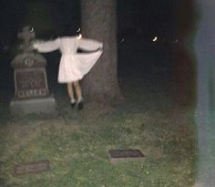 a woman standing in front of a grave at night with her arms spread wide out