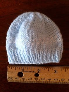 a white knitted hat sitting on top of a wooden table next to a ruler