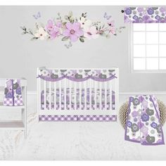 a baby crib bedding set with purple and white flowers on the wall next to it