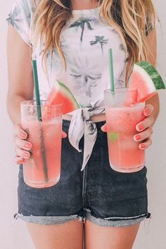 a woman holding two watermelon drinks in her hands