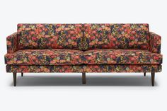 an upholstered floral couch with wooden legs and arm rests against a white background